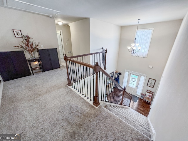 stairway featuring attic access, a chandelier, and carpet