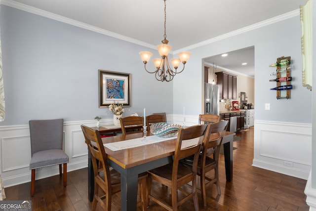 dining room with a chandelier, dark wood-style floors, ornamental molding, a wainscoted wall, and a decorative wall