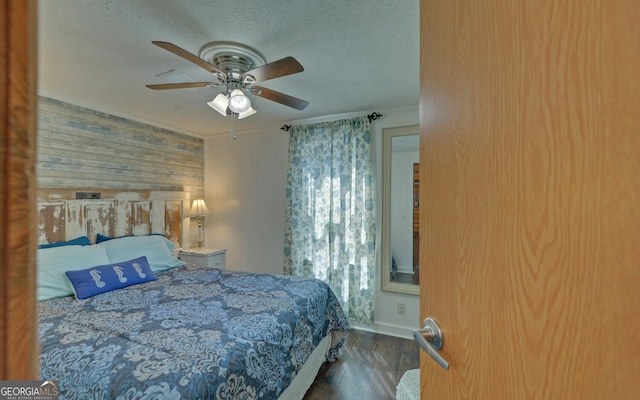 bedroom featuring wood finished floors, wood walls, a textured ceiling, a ceiling fan, and baseboards