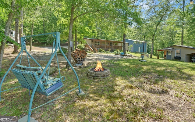 view of green lawn with a fire pit, a playground, and a wooden deck