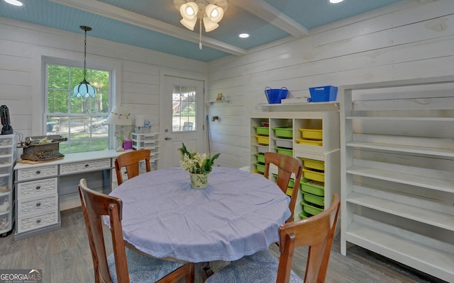 dining area featuring wood finished floors, wood walls, beamed ceiling, ceiling fan, and plenty of natural light