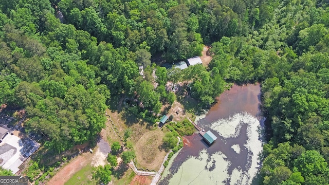 aerial view of property and surrounding area with a nearby body of water and a heavily wooded area