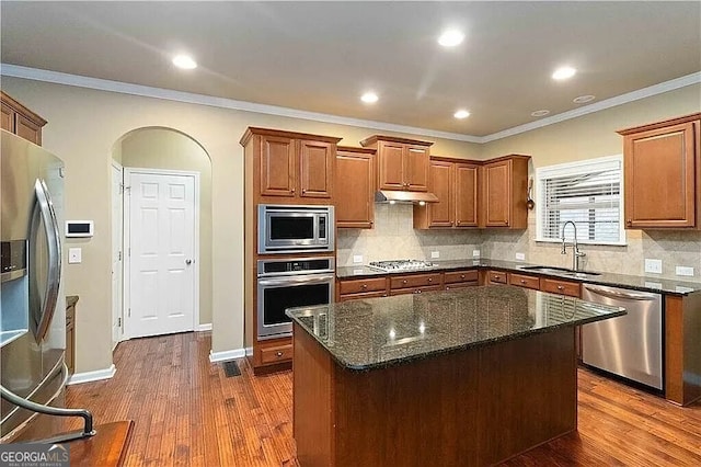 kitchen featuring stainless steel appliances, a sink, brown cabinetry, decorative backsplash, and crown molding