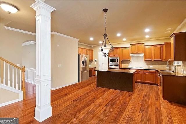 kitchen featuring stainless steel appliances, crown molding, a sink, dark wood-style floors, and a kitchen island