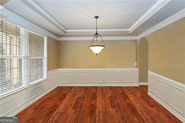 spare room with a raised ceiling, hardwood / wood-style flooring, arched walkways, wainscoting, and ornamental molding