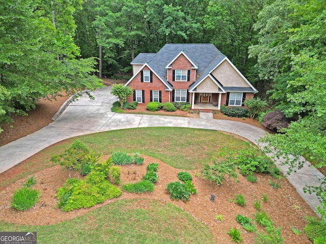 view of front facade featuring curved driveway, a front yard, covered porch, and brick siding