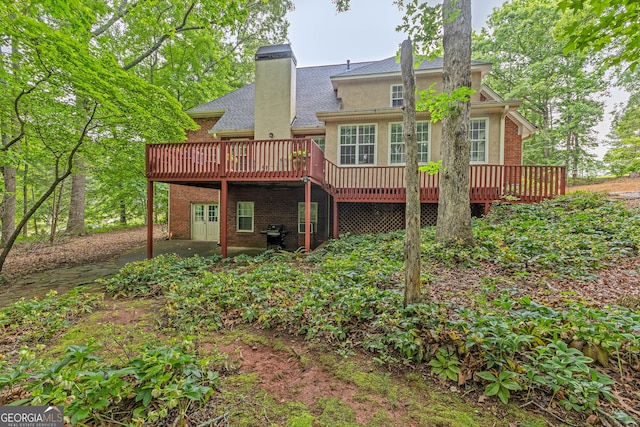rear view of property featuring a deck, roof with shingles, a chimney, brick siding, and a patio area
