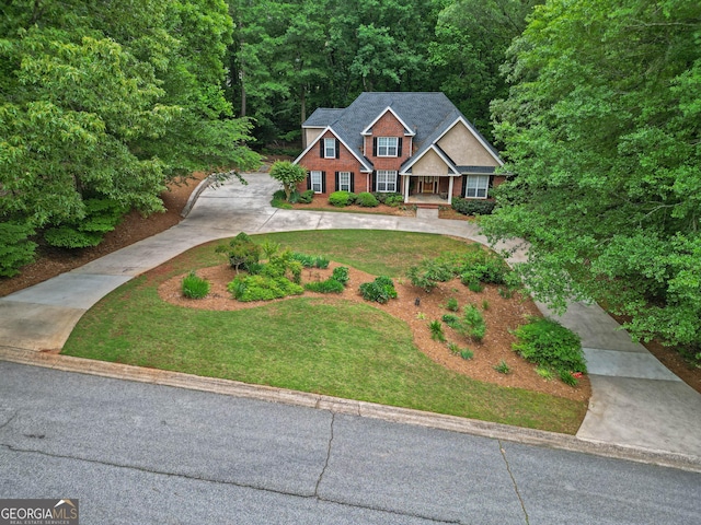 view of front of property featuring a front lawn, driveway, and a view of trees