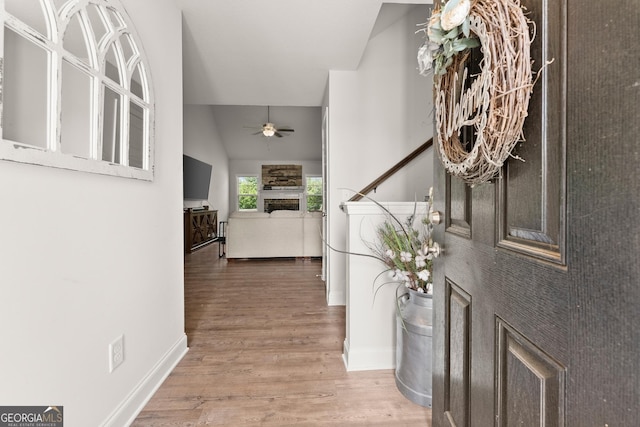 entryway featuring a ceiling fan, wood finished floors, baseboards, and vaulted ceiling