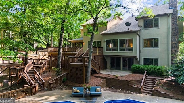 back of house with stairway, a wooden deck, a patio, stucco siding, and roof with shingles