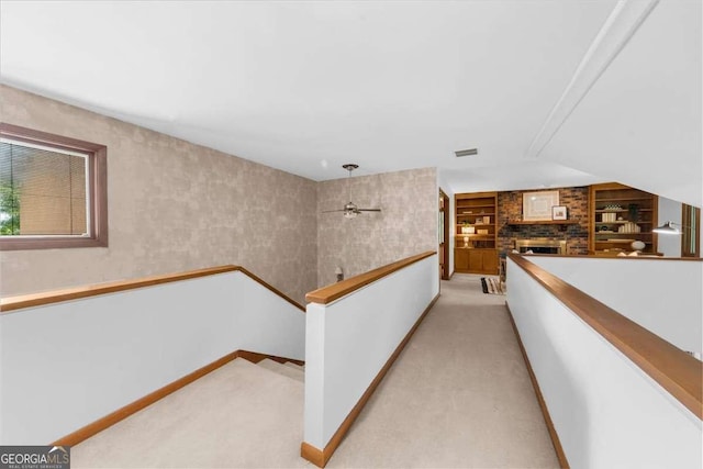 corridor featuring an upstairs landing, light colored carpet, built in features, and baseboards