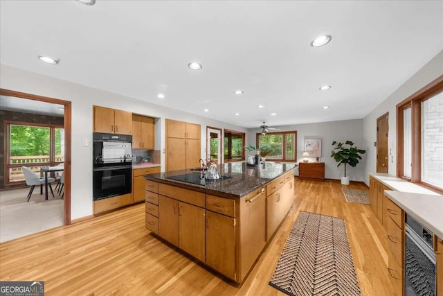 kitchen with black appliances, light wood-style flooring, plenty of natural light, a center island, and recessed lighting