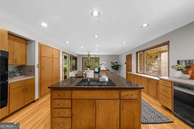 kitchen featuring black appliances, light wood-style flooring, a sink, recessed lighting, and backsplash