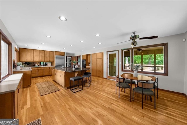 kitchen with stainless steel refrigerator, brown cabinets, a kitchen bar, light wood-style flooring, and a kitchen island with sink