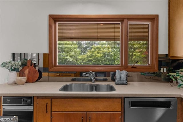 kitchen with stainless steel dishwasher, a sink, light countertops, and brown cabinets