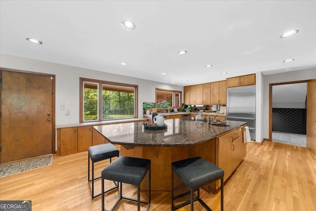 kitchen with built in refrigerator, brown cabinetry, a sink, light wood-type flooring, and a center island