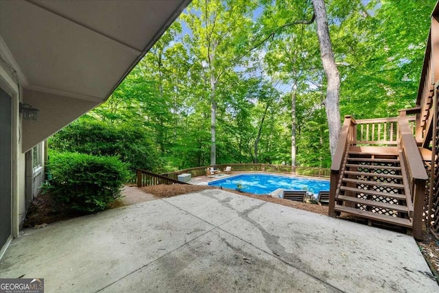 outdoor pool with a patio, stairway, a wooden deck, and view of scattered trees