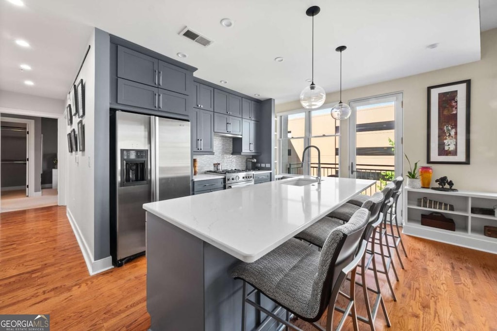 kitchen with appliances with stainless steel finishes, a sink, light wood-style floors, a large island with sink, and recessed lighting