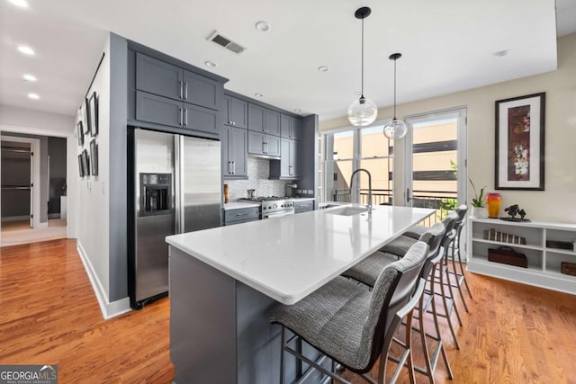 kitchen with appliances with stainless steel finishes, a sink, light wood-style floors, a large island with sink, and recessed lighting
