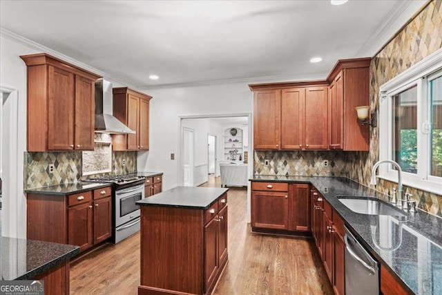 kitchen with stainless steel appliances, wall chimney range hood, a sink, wood finished floors, and ornamental molding