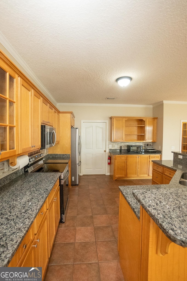 kitchen with appliances with stainless steel finishes, open shelves, crown molding, dark stone countertops, and dark tile patterned floors
