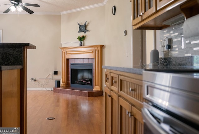 living room featuring ceiling fan, a fireplace, wood finished floors, crown molding, and baseboards