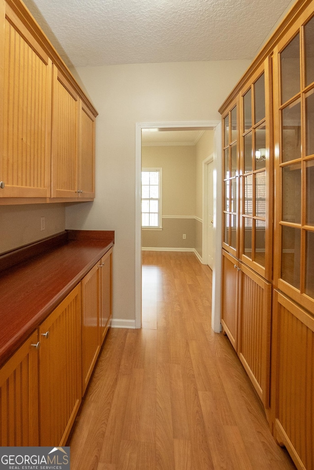 corridor with light wood-style floors, a textured ceiling, and baseboards