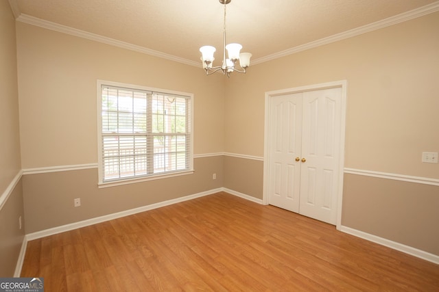 empty room featuring light wood-style floors, a chandelier, crown molding, and baseboards