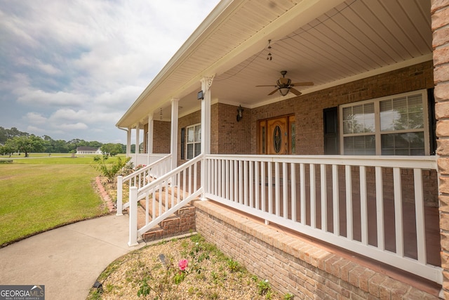 doorway to property with a lawn, a porch, ceiling fan, and brick siding