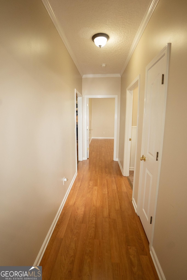 hall with a textured ceiling, wood finished floors, baseboards, and crown molding