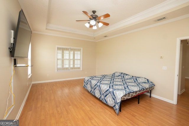 bedroom with wood finished floors, a tray ceiling, crown molding, baseboards, and ceiling fan