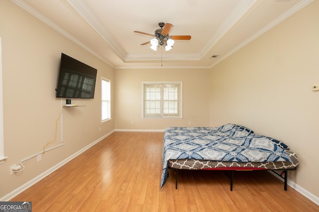 bedroom with a tray ceiling, wood finished floors, crown molding, baseboards, and ceiling fan