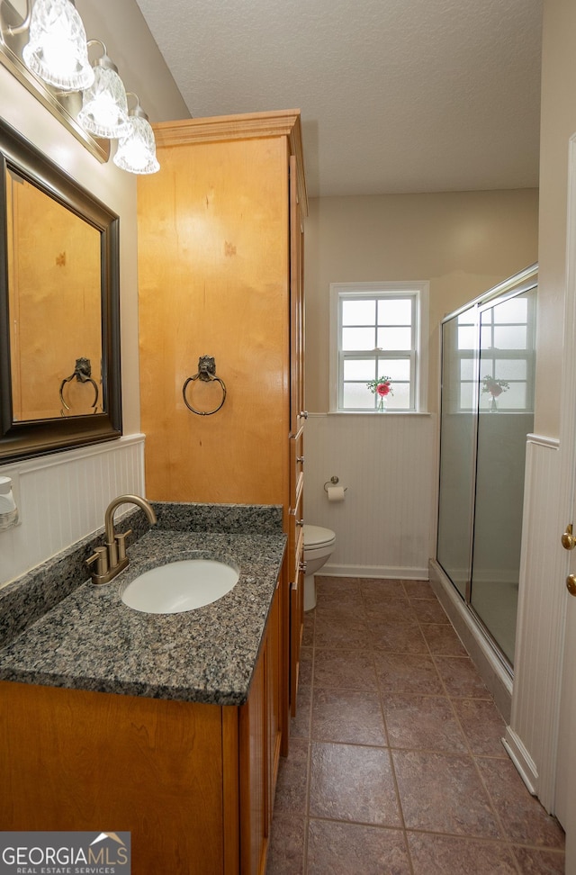 bathroom featuring a stall shower, toilet, vanity, and a wainscoted wall