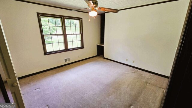 empty room featuring light carpet, ceiling fan, a textured ceiling, baseboards, and ornamental molding