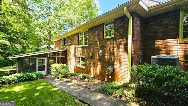 view of side of home with a sunroom, central AC unit, and brick siding