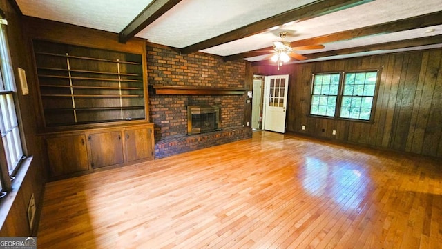 unfurnished living room with wood-type flooring, wood walls, beamed ceiling, a brick fireplace, and ceiling fan