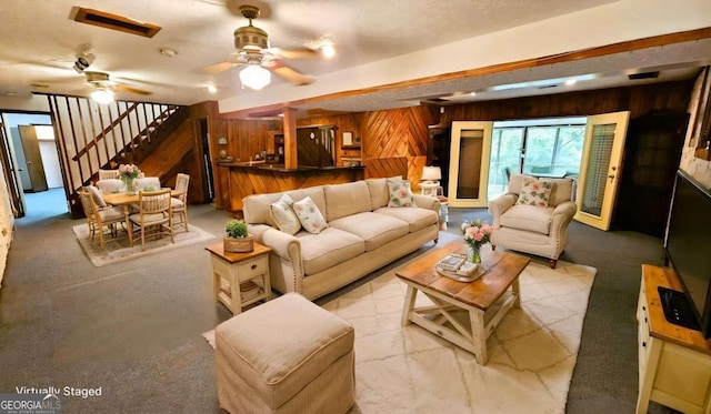 living room featuring wooden walls, stairs, a ceiling fan, bar area, and carpet floors
