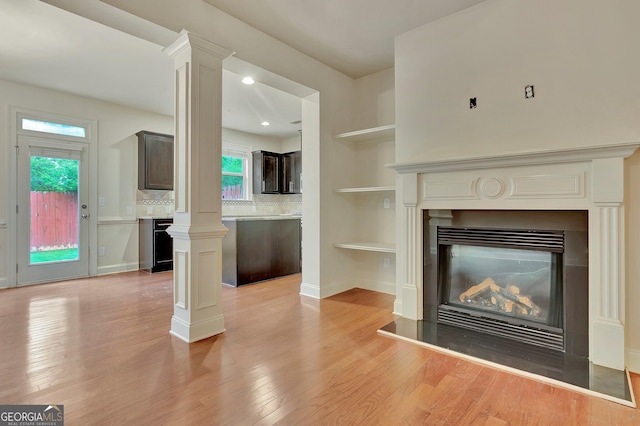 unfurnished living room featuring decorative columns, light wood finished floors, and a glass covered fireplace