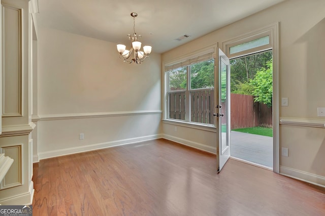 unfurnished dining area with wood finished floors, a chandelier, and baseboards