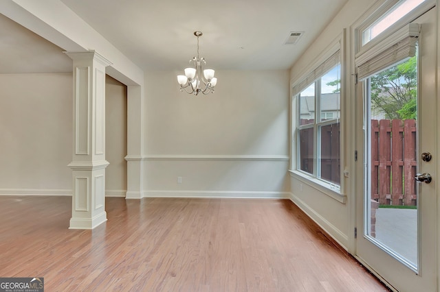 unfurnished dining area featuring decorative columns, light wood-type flooring, a chandelier, and baseboards