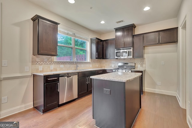 kitchen featuring stainless steel appliances, a sink, dark brown cabinets, light wood-style floors, and backsplash