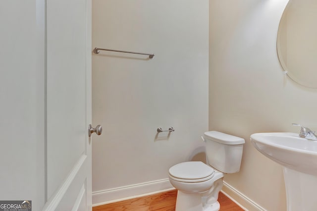 half bath with wood finished floors, toilet, baseboards, and a sink