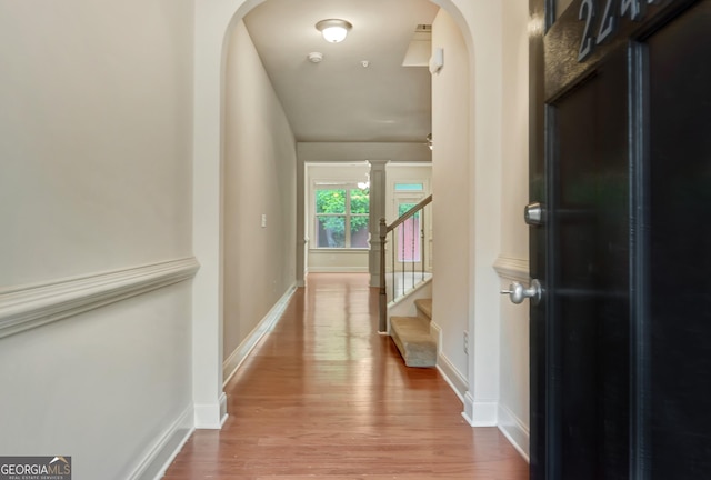 hallway featuring arched walkways, wood finished floors, baseboards, and stairway