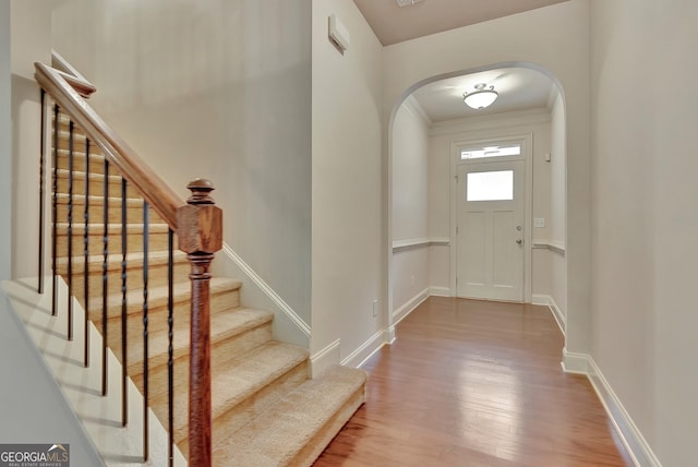 foyer entrance featuring arched walkways, wood finished floors, stairs, crown molding, and baseboards