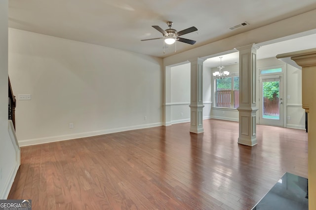 empty room featuring ornate columns, wood finished floors, a ceiling fan, a chandelier, and baseboards