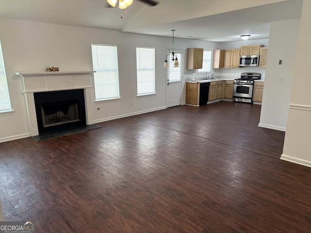 unfurnished living room with a sink, a ceiling fan, dark wood finished floors, baseboards, and a fireplace with raised hearth