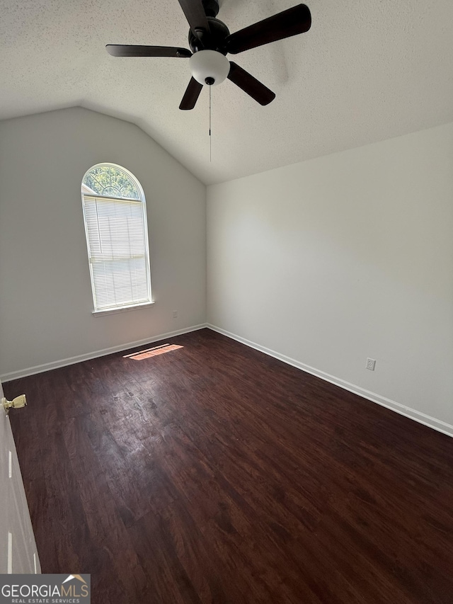 empty room featuring lofted ceiling, dark wood-style flooring, a textured ceiling, baseboards, and ceiling fan