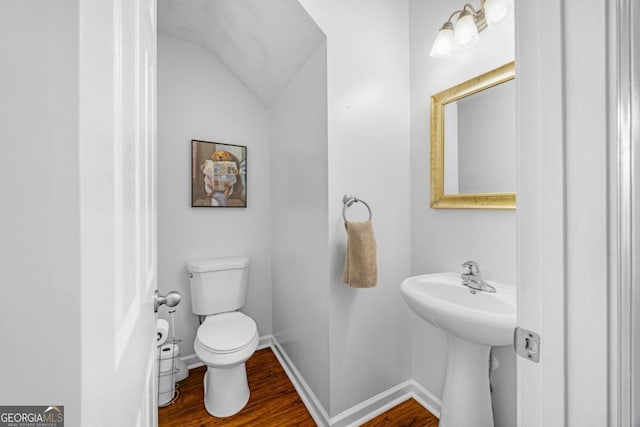 half bath featuring wood finished floors, toilet, lofted ceiling, baseboards, and a sink