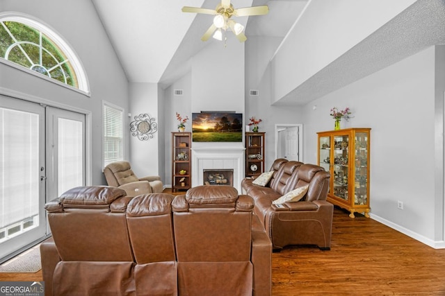 living room featuring wood finished floors, baseboards, high vaulted ceiling, a ceiling fan, and a tile fireplace