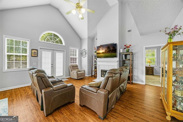 living area with high vaulted ceiling, ceiling fan, a tile fireplace, french doors, and wood finished floors